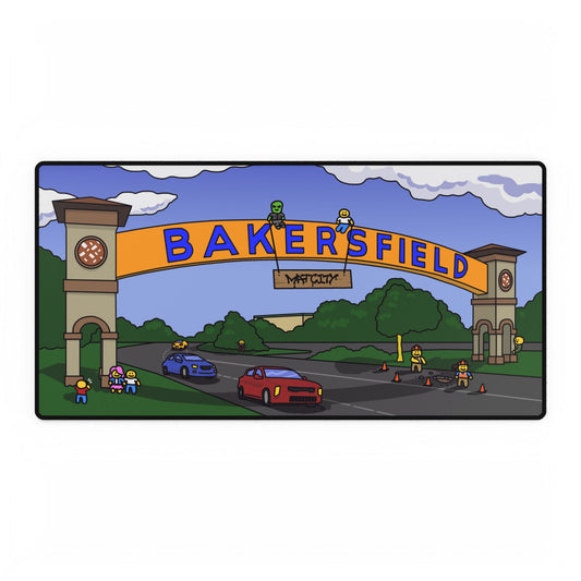 Wide desk‑pad illustration of Bakersfield’s iconic archway, two clock towers and rolling clouds above a road with red and blue cars, tiny construction workers, trees and Matcity tag.