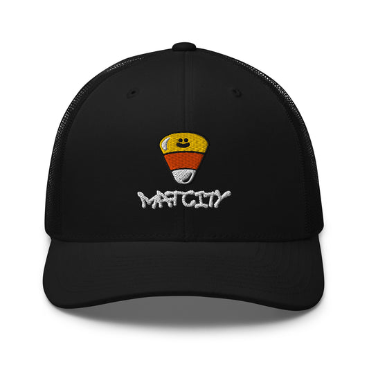 A black trucker cap with mesh back featuring an embroidered candy corn and white Matcity graffiti logo on the front, with a curved brim.