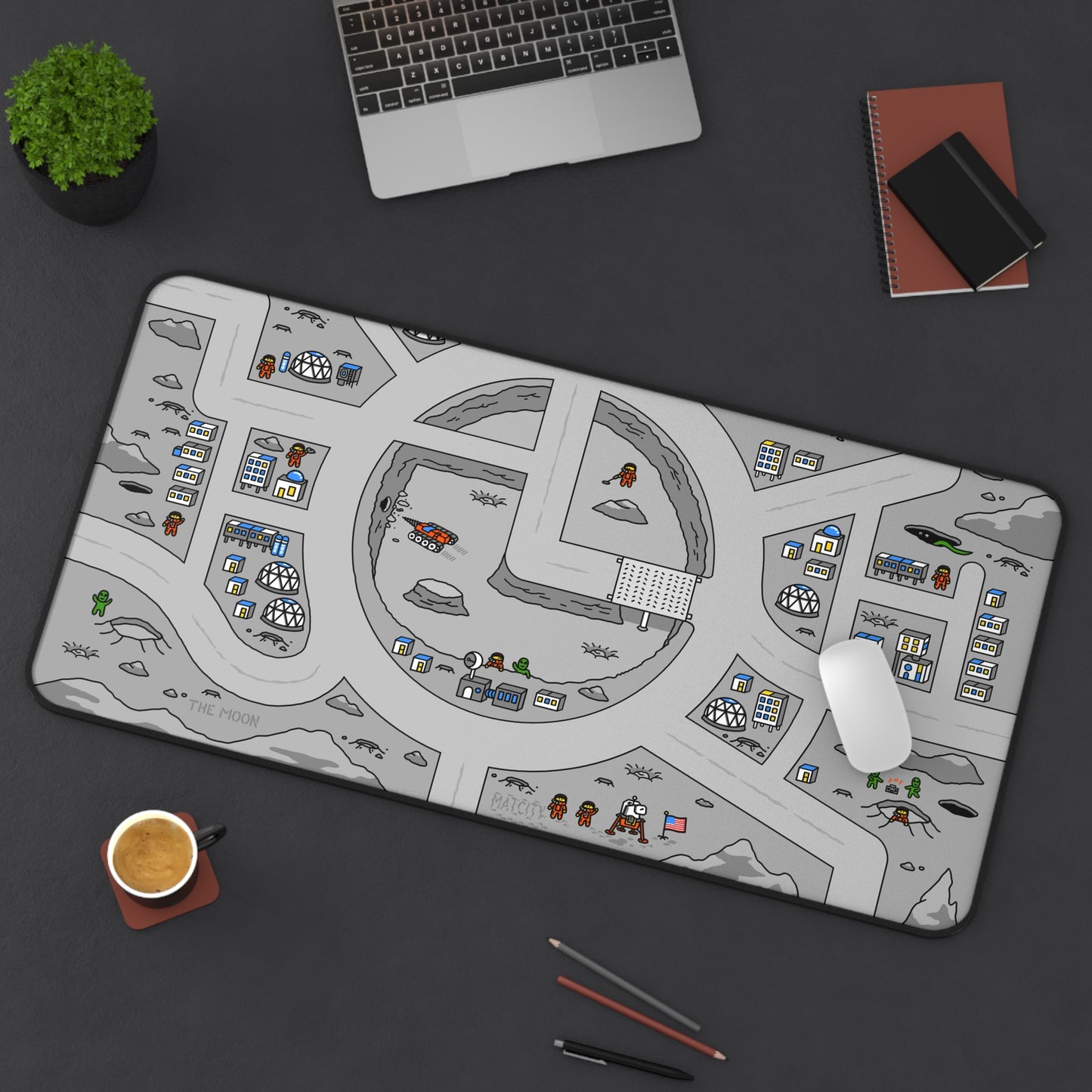 Matcity Moon Mat Large placed on a desk with a laptop, mouse, and notebooks, highlighting the detailed lunar design with buildings and astronauts.
