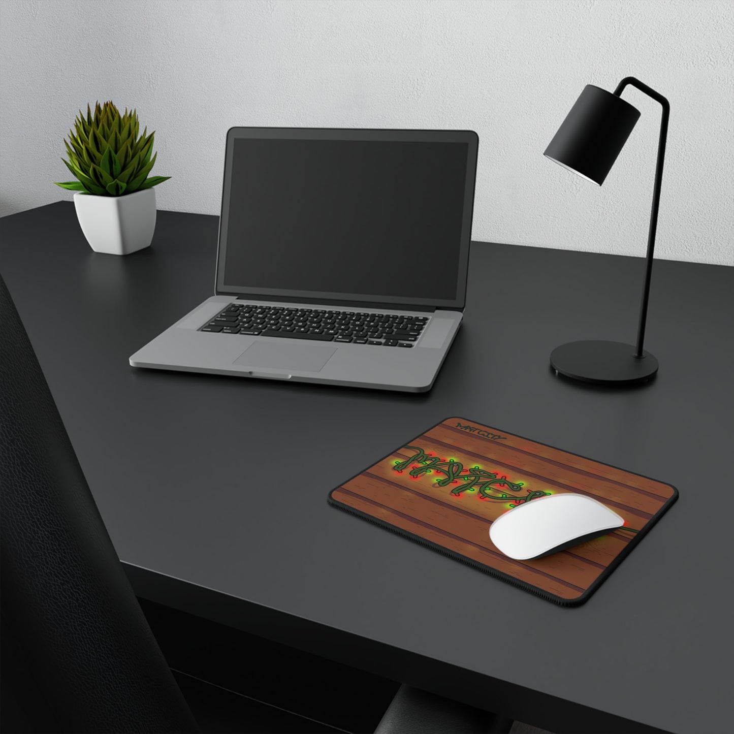 The mouse pad on a dark desk setup with a laptop, lamp, and plant, highlighting its compact and festive design.