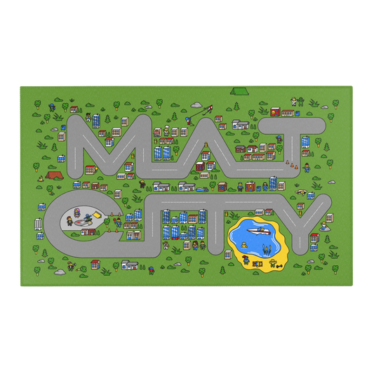 An overhead view of a green play mat designed in the shape of the word 'Matcity,' with roads forming the letters. The mat is filled with colorful, cartoon-style illustrations of buildings, people, trees, and vehicles. Notable elements include a helicopter landing pad with people nearby, a kite flyer, a pond with a boat, and various homes and skyscrapers scattered across the mat. The scene is lively, with small characters engaged in activities like construction, playing, and camping.