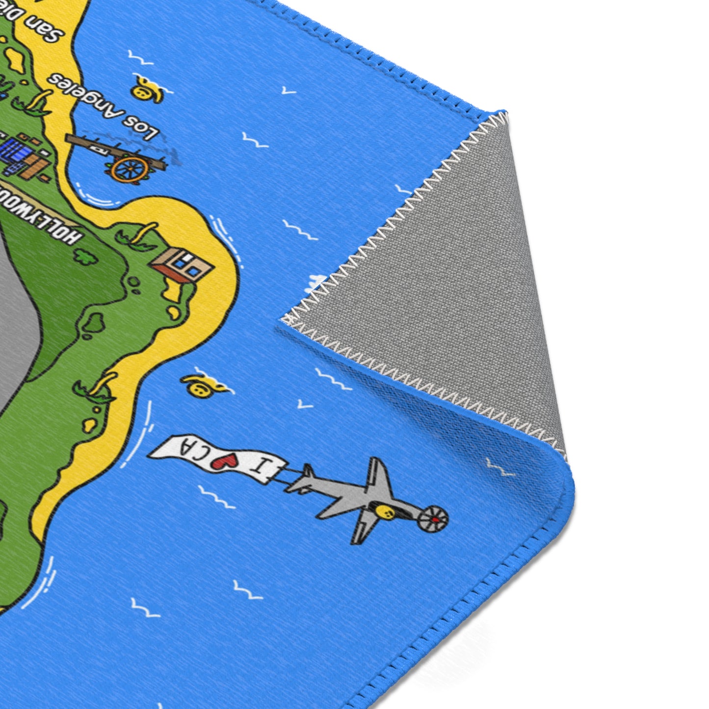 Close-up of the Matcity California Mat showing a stitched edge and a small plane towing a banner that reads “I ❤️ CA” over the Pacific Ocean.