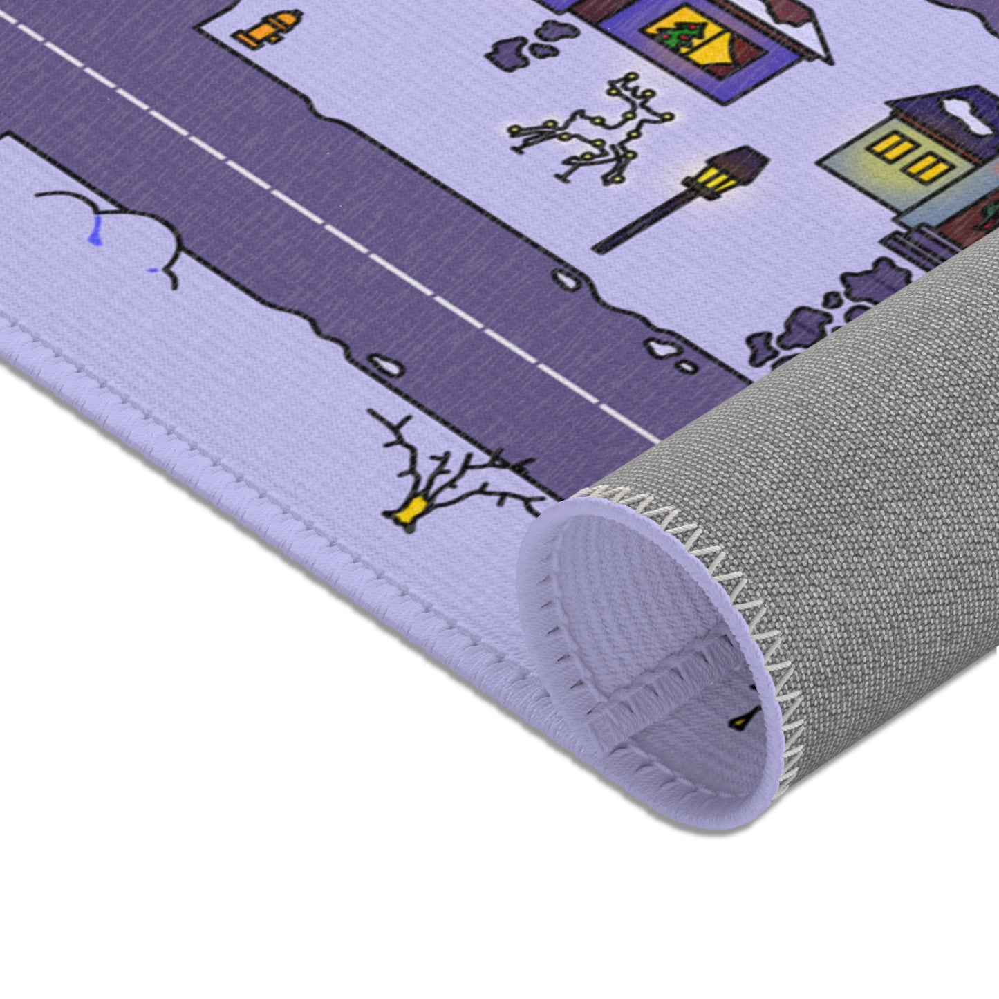 Rolled mat end revealing non slip gray backing, top side with snowy road, bare trees and yellow lit cottage roofs.