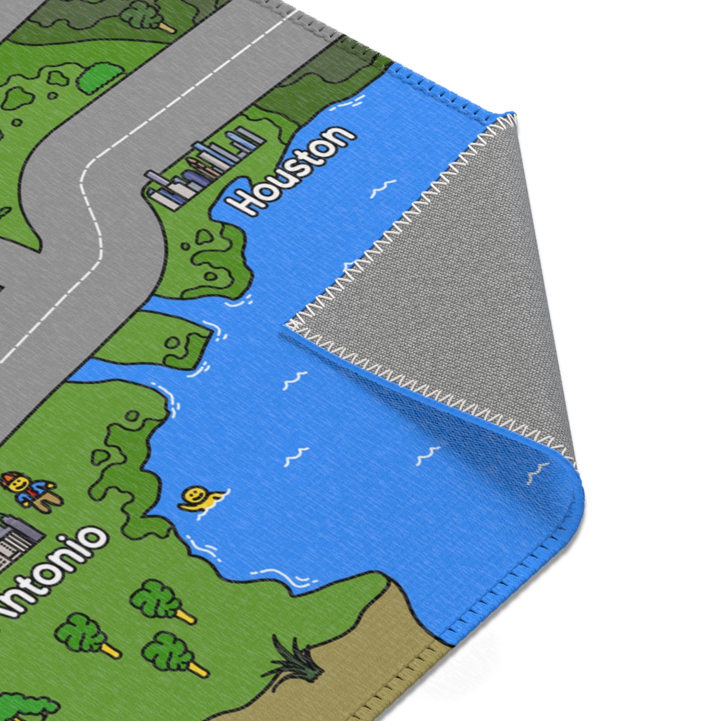 Close-up of mat corner showing blue Gulf water by Houston, neatly stitched white edging, and the grey, textured rubber backing revealed by a fold.