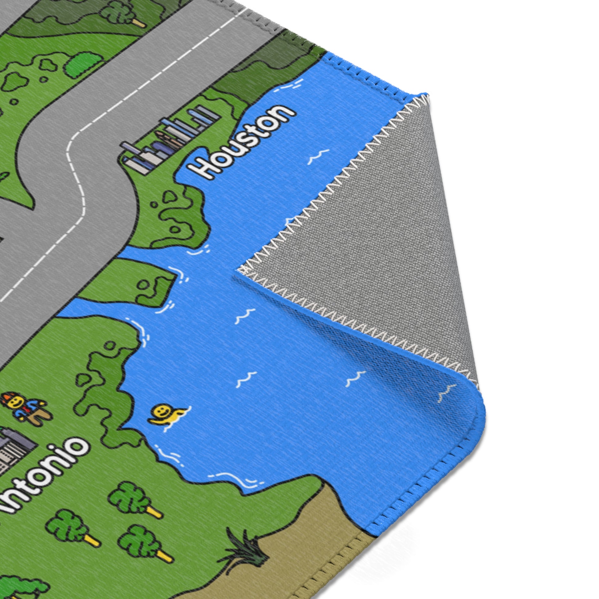 Close-up of mat corner showing blue Gulf water by Houston, neatly stitched white edging, and the grey, textured rubber backing revealed by a fold.