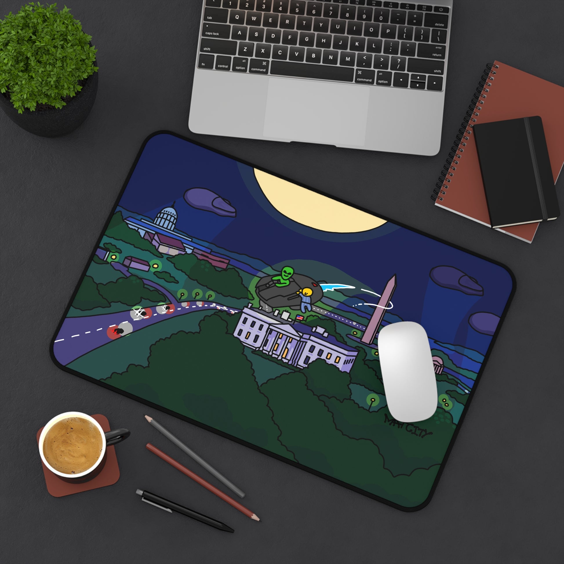 The Matcity alien-themed mouse mat placed on a dark desk alongside a laptop, notepad, and coffee cup, adding a playful yet sleek touch to the workspace.